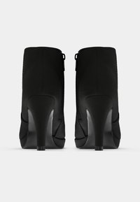 Botines negros de tacón alto con una textura suave, con una cremallera en la parte trasera y un tacón cónico. Silueta sencilla, sin adornos.