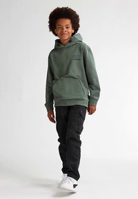 Felpa con cappuccio in verde scuro, con tasca a marsupio frontale, dettagli stampati, abbinata a pantaloni cargo neri e sneakers bianche.