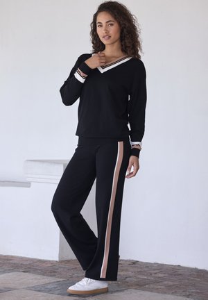 Black long-sleeve top with a V-neck and white and brown stripes, paired with black pants featuring a brown side stripe, completed with white shoes.