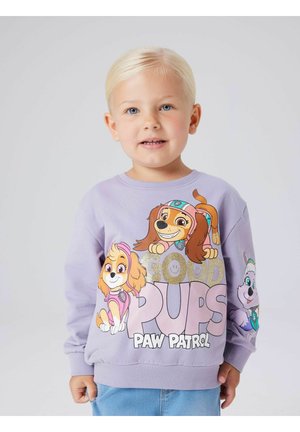 Lyse lilla genser med tegneseriehunder fra Paw Patrol, med teksten "GOOD PUPS" i store, fete, glitrende bokstaver. Rund hals og ribbestrikkede mansjetter.