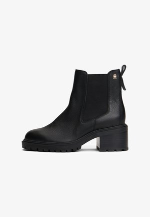 Bota de tornozelo em couro preto com acabamento texturizado, painéis laterais elásticos e salto bloco. Apresenta uma alça de puxar e detalhe em metal com o logo na lateral.