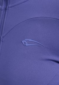 Lilla atletisk top i glat og strækbar stof, med et sømløst design og en diskret logo accent på venstre side.