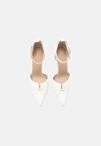 Bijele štikle s špicastim nožnim dijelom i remenom oko gležnja, s naglašenim naboranim dizajnom i malim izrezom sprijeda, glatke teksture.