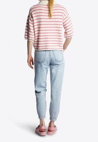 Gestreepte oversized trui in crème en roze, blauwe jeans en roze instapschoenen. Zichtbare achterkant met korte mouwen en geribbelde halslijn.