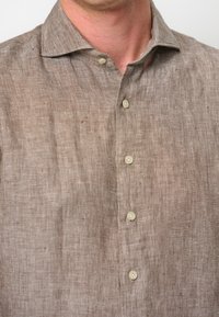 Camicia di lino marrone chiaro con colletto a bottoni, tessuto testurizzato con trama visibile e sei bottoni color crema lungo la parte anteriore.