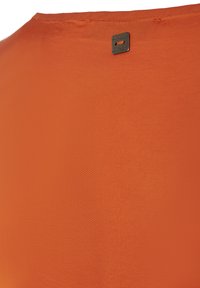 Camicia di tessuto arancione con una texture liscia. Presenta un'etichetta nera con logo del marchio in rilievo vicino al colletto. Design semplice e minimalista.