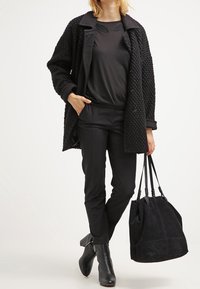 Abrigo negro texturizado con un cuello, camisa negra con detalles en relieve, pantalones ajustados y botines. Bolso tote de ante negro.