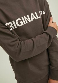 Felpa marrone con scritta bianca "ORIGINAL", polsini a costine e una texture morbida, caratterizzata da maniche lunghe e una vestibilità rilassata.