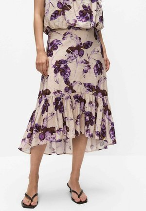 Beige bloemenrok met paarse en bruine bladeren en een geplooide zoom, gedragen met een bijpassende top en zwarte sandalen met hak op een witte achtergrond.