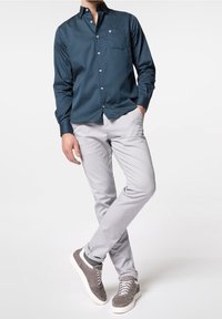 Námořnická košile s knoflíky a bílými puntíky, šedé slim-fit kalhoty a šedé tenisky s bílou podrážkou. Elegantní provedení a přiléhavý styl.