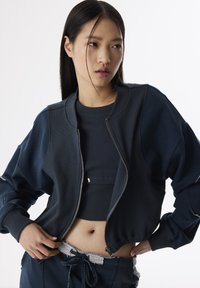 Marine groen bomberjack met ritssluiting, geribbelde textuur en oversized mouwen, gecombineerd met een bijpassend crop top en oversized broek.