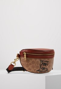 Brun canvasväska med gyllene detaljer, dragkedjestängning, läderaccenter och en djärv svart grafisk design på framsidan. Justerbar rem ingår.