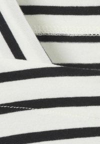 Schwarz-weißer gestreifter Stoff, der eine weiche, gerippte Textur zeigt. Verfügt über einen V-Ausschnitt mit sichtbaren Steppdetails an den Kanten.