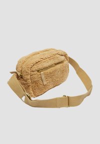 Beige Plüsch-Crossbody-Tasche mit strukturiertem Oberflächenmaterial, zwei Reißverschlussfächern und einem breiten, verstellbaren Stofftrageriemen. Akzente in goldfarbener Hardware.