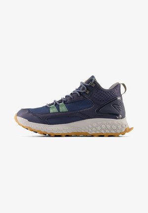Navy hiking shoe with textured fabric, mesh panels, and green accents. Thick, grey sole with hexagonal patterns and a rubber grip.