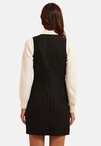 Abito nero a righe sottili realizzato in tessuto testurizzato, con un design aderente e senza maniche, abbinato a un maglione crema a trecce.