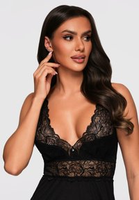 Lingerie in pizzo nero con design a scollo profondo a V, motivi floreali e un bottone decorativo al centro. Tessuto morbido e trame a strati.