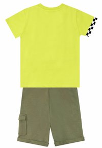Camiseta amarilla neón con acento de cuadros negros en la manga, combinada con pantalones cortos verde oliva con un bolsillo lateral y puños doblados.