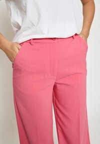 Roza široka hlače z gladko teksturo, ki imajo stranske žepke in prilegajoč pas z gumbom.