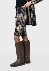 Granatowa spódnica w kratkę do kolan z beżowymi liniami, zestawiona z wysokimi, ciemnobrązowymi skórzanymi botkami na płaskiej podeszwie i minimalnymi detalami.