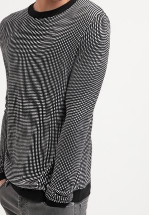 Pull à manches longues noir et blanc à motif, avec un col rond, des bords-côtes aux poignets et une coupe ajustée, présentant une texture en quadrillage sur l'ensemble.
