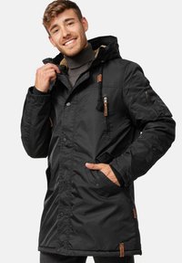 Schwarze wasserdichte Jacke mit einem pelzigen Kapuzenfutter, Druckknöpfen und seitlichen Reißverschlusstaschen. Verfügt über braune Lederakzente an den Reißverschlüssen.