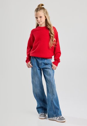 Red knitted sweater with a round neckline, paired with wide-leg blue jeans featuring vertical stitching. Gray sneakers with white soles.