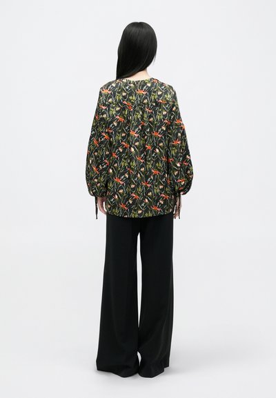 Juostos su gėlių raštu juodoje medžiagoje, su ilgomis rankovėmis, raukšlėmis ir raišteliais, derinamos su laisvomis juodomis kelnėmis.