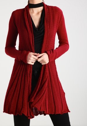 Bordeauxrode, langarmige cardigan met ribbelstructuur, open voorkant, gedrapeerd ontwerp en uitlopende zoom. Gecombineerd met een zwart shirt en zwarte broek.