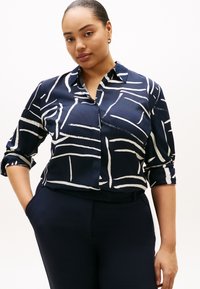 Μπλούζα σε ναυτικό μπλε χρώμα από λείο ύφασμα με άσπρα αφηρημένα γραμμικά σχέδια, διαθέτει γιακά και μανίκια γυρισμένα προς τα πάνω. Συνδυάζεται με παντελόνι σε ναυτικό μπλε χρώμα.