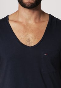 Granatowa koszulka z dekoltem w serek, wykonana z miękkiego materiału, z małą kieszonką z akcentem logo i luźnym krojem.