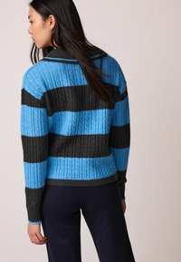 Sweter w paski wykonany z teksturowanej dzianiny, z niebieskimi i ciemnoszarymi poziomymi paskami, prążkowanym dołem i długimi rękawami.