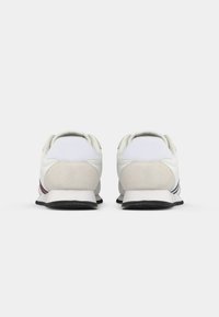 Scarpe sportive bianche con tomaia in pelle liscia e suede, dotate di un colletto imbottito e suole in gomma nere con strisce grigie e rosse.