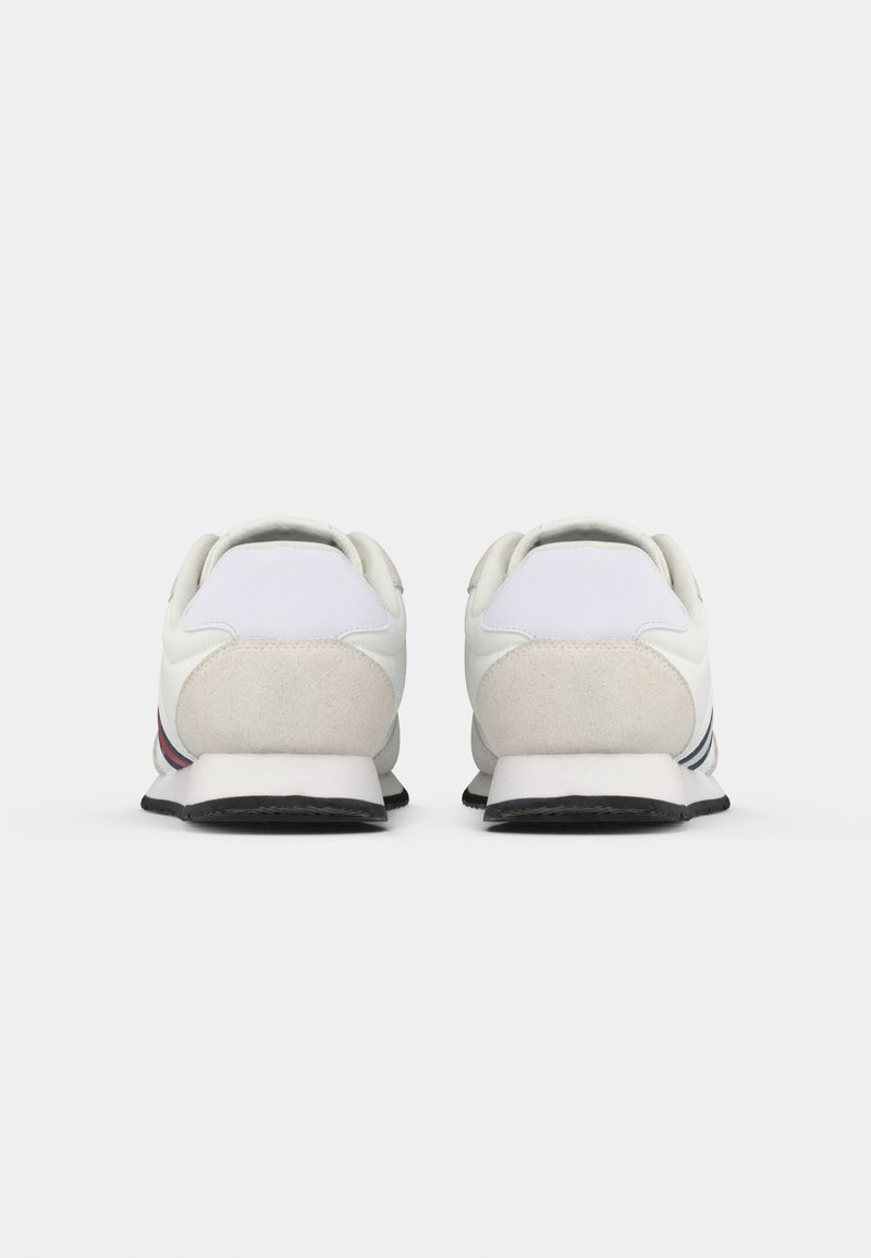 Zapatillas deportivas blancas con una parte superior de cuero y ante suave, que cuentan con un collar acolchado y suelas de goma negra con franjas grises y rojas.