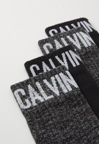 Trys kojinių poros juodos ir pilkos spalvų atspalvių, su briaunotu tekstūromis ir dideliu baltu "CALVIN" logotipu viršuje.