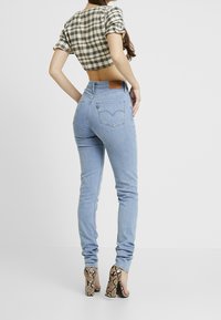 Jeans ajustados de color azul claro con un ajuste de cintura alta, con bolsillos traseros y una etiqueta de cuero marrón. Combinados con un top corto a cuadros en blanco y negro.