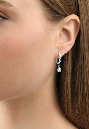 Orecchino a cerchio in argento con design a goccia, caratterizzato da una pietra preziosa chiara e sfaccettata a forma di goccia. Texture liscia e finitura lucida.