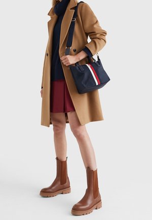 Ruske nahkne čevlje z elastičnima stranskima paneloma, debelim podplatom in nizko peto; kombinirani s kameljnim plaščem in temnimi dodatki.