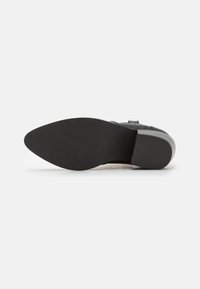 Černá podrážka boty s hladkým, texturovaným gumovým povrchem, tvarovaná se zakřivením a malým podpatkem. Na povrchu jsou jemné vlnité vzory.