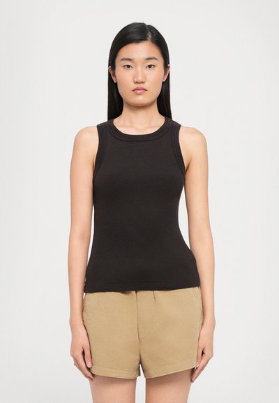 Top negro de canalé con escote redondo, forma ajustada y textura suave, presentado con pantalones cortos beige en un entorno casual.