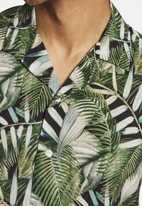 Kortærmet skjorte i sort med mønstre af grønne blade og palmeblade. Har krave og detaljer med knapper foran. Glat stoffet struktur.