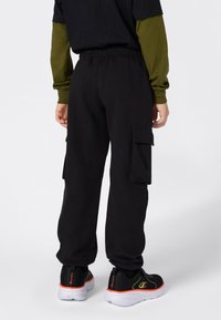 Zwarte cargobroek met zijzakken, elastische tailleband en omgeslagen hemden. Gecombineerd met zwarte sneakers met oranje accenten.