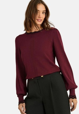Burgunderfarbene Bluse mit langen Ärmeln, gerippter Textur und schwarzem, gewelltem Kragen. Verfügt über puffige Ärmel mit schwarzen Akzenten.