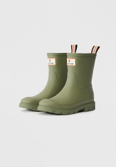 Botas de chuva verdes de borracha com acabamento suave, design de tornozelo alto e etiqueta de marca acentuada em laranja com um logótipo de raposa na frente.