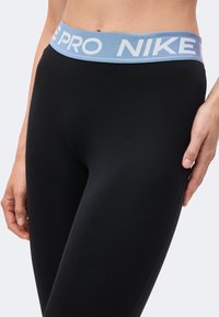 Gros plan d'une personne portant un legging noir avec une ceinture bleu clair sur laquelle est imprimé "NIKE PRO" en lettres blanches.