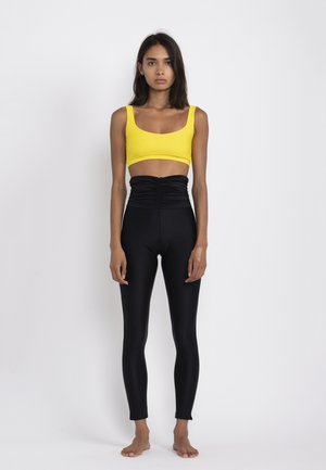 Yellow cropped top with a wide neckline, paired with high-waisted black leggings featuring gathered detail on the front. Smooth texture.