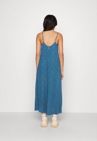 Modrá maxi šaty s květinovým vzorem, nastavitelnými tenkými ramínky a kulatým zadním dílem, doplněné světle zbarvenými chunky teniskami.