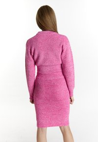 Rochie tricotată în roz aprins, cu o textură ribbed. Dispune de mâneci lungi, o siluetă ajustată și un design care accentuează talia.