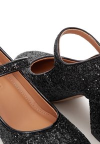 Černé třpytivé lodičky s uzavřenou špičkou, nastavitelným páskem a zakřiveným výřezem. Hladká vnitřní podšívka a masivní podpatek.