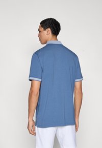 Μπλε μπλουζάκι πόλο με κοντά μανίκια και αντίθετο γιακά και μανσέτες. Ομαλή υφή, χαλαρή εφαρμογή και ίσια βάση με πλαϊνές σχισμές.